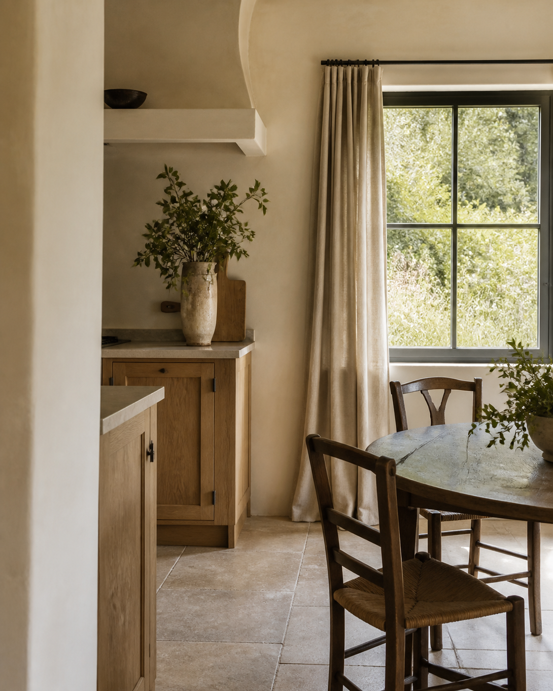 A round wooden dining table and rush-seated chairs beside a curved plaster archway leading to a kitchen counter