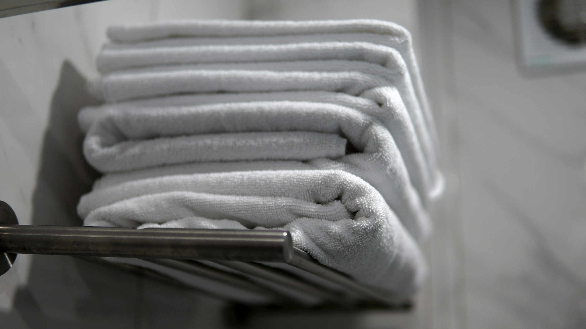 A stack of folded white bath towels resting on a chrome towel rail against grey-veined marble tile